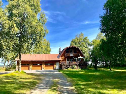 A rustic log cabin with a red roof, surrounded by trees and a grassy area, under a blue sky.