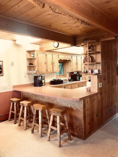 Cozy wooden kitchen with a bar area, featuring stools, cabinets, and appliances in a warm, rustic setting.