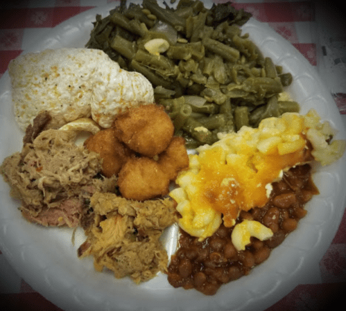 A plate of food featuring pulled pork, green beans, macaroni and cheese, baked beans, and corn fritters.