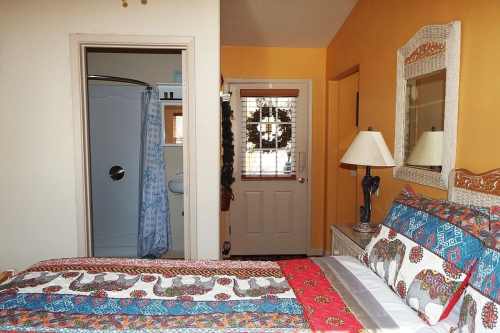 Cozy bedroom with a colorful quilt, a lamp, and a door leading to a bathroom with a shower curtain.