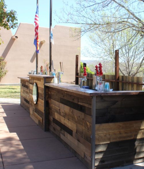 Outdoor bar area with wooden counters, flags, and a clear blue sky in the background.