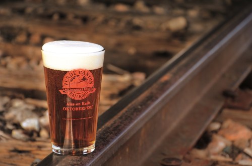 A pint of amber beer with a frothy head sits on a railway track, featuring a logo for Oktoberfest.