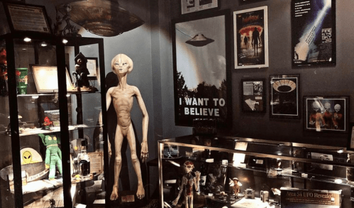 A display featuring alien figures, UFO memorabilia, and posters, including "I Want to Believe."