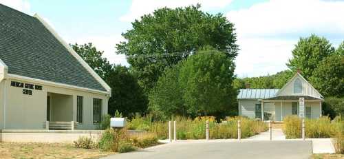 Two buildings in a green landscape: a modern center on the left and a quaint house on the right, surrounded by trees and plants.