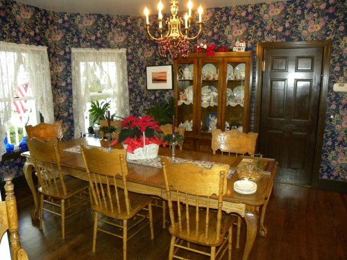 A cozy dining room with floral wallpaper, a wooden table set for dinner, and a chandelier overhead.