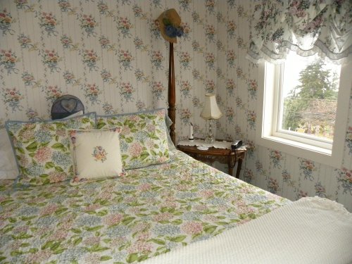 Cozy bedroom with floral wallpaper, a quilted bedspread, and a window letting in natural light.