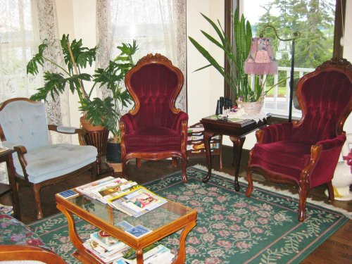 A cozy living room with two ornate velvet chairs, a glass coffee table, and plants, surrounded by natural light.