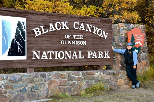 A park ranger stands next to the Black Canyon of the Gunnison National Park sign, surrounded by autumn foliage.