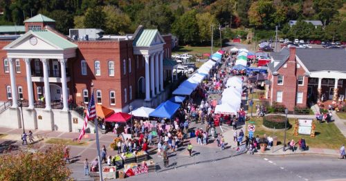 Aerial view of a bustling outdoor market with colorful tents, people, and historic buildings in the background.