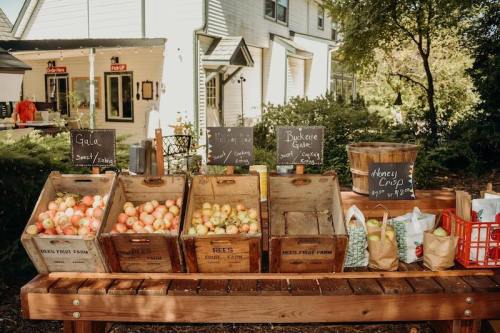 A wooden stand displays crates of apples and signs for different varieties at a farm market.