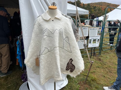 A white poncho with mountain designs and a bear motif displayed on a mannequin at an outdoor market.