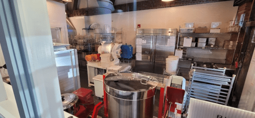 A view of a commercial kitchen with various equipment, including mixers, refrigerators, and storage shelves.