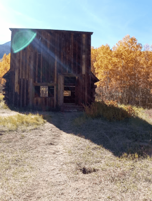 A rustic wooden building surrounded by vibrant autumn foliage and a clear blue sky.