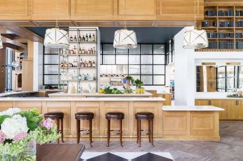 A modern bar with wooden cabinetry, stylish pendant lights, and a variety of drinks displayed on shelves.