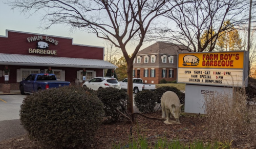 Exterior of Farm Boy's Barbeque with a sign displaying hours and specials, surrounded by shrubs and a tree.