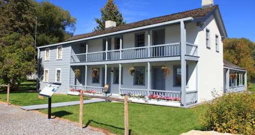 A two-story house with blue and white siding, featuring balconies, flower boxes, and a grassy area in front.