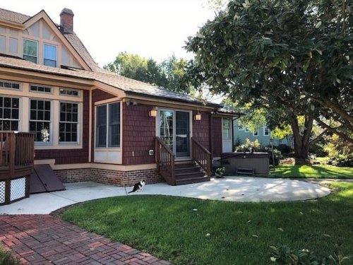 A charming house with a porch, surrounded by greenery and a small cat on the lawn.