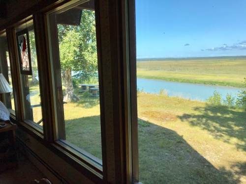 A view from a window showing a grassy landscape and a river under a clear blue sky.