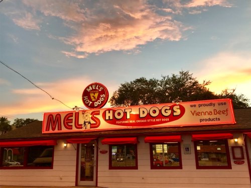 A colorful sunset behind Mel's Hot Dogs, featuring a sign that highlights Vienna Beef products.