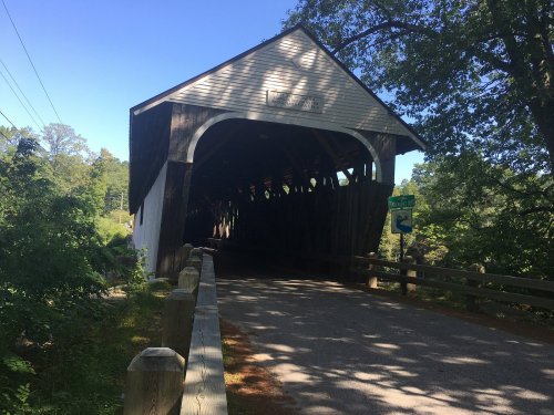 A scenic view of a covered bridge surrounded by trees and a clear blue sky.