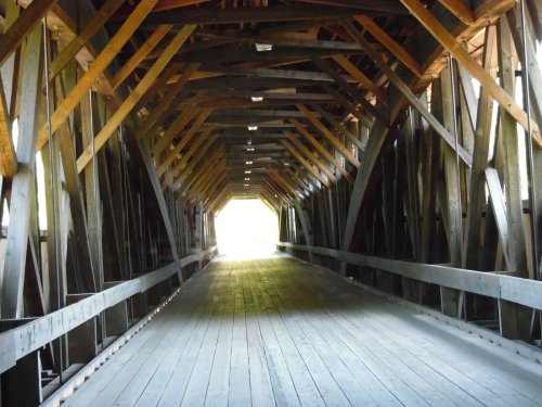 A wooden covered bridge interior with a light-filled exit at the end, showcasing intricate wooden beams.