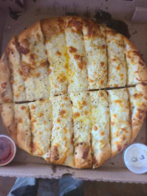 A round cheese pizza with golden crust, sliced into pieces, accompanied by two small containers of dipping sauce.
