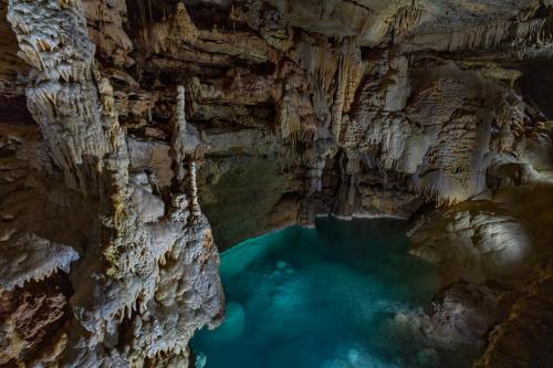 A stunning underground cave with stalactites and stalagmites surrounding a clear blue pool of water.