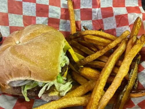 A hamburger with lettuce on a bun, served with a side of golden-brown sweet potato fries on a red-checkered paper.