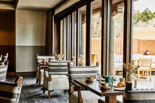 Cozy dining area with wooden tables, striped chairs, and large windows overlooking an outdoor space.