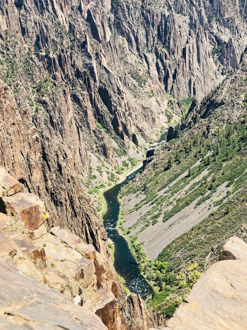 Aerial view of a winding river surrounded by steep, rocky cliffs and lush greenery in a canyon landscape.