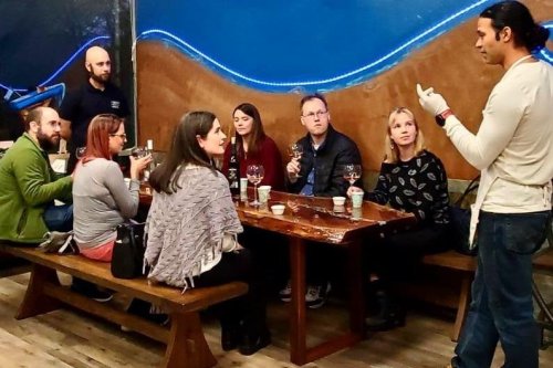 A group of people seated at a table, listening to a speaker while enjoying drinks in a cozy setting.