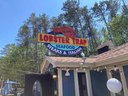 Sign for "Lobster Trap" restaurant featuring seafood, steaks, and Italian cuisine, surrounded by trees.