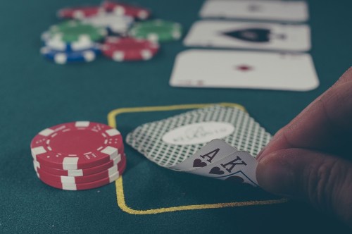 A hand reveals two aces over a poker table with chips and playing cards in the background.