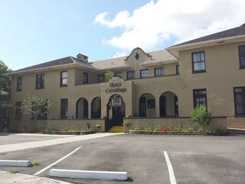 Historic hotel building with arched entrance, yellow steps, and landscaped front, set against a blue sky.