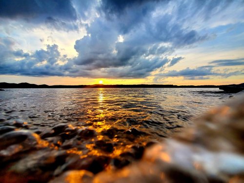 A serene sunset over calm waters, with dramatic clouds reflecting golden hues in the sky.