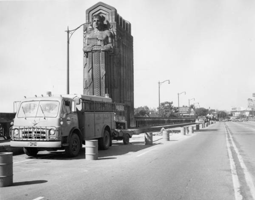 A vintage truck parked near a large, decorative stone monument on a city street.