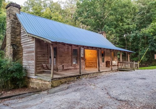A rustic wooden cabin with a blue metal roof, surrounded by trees and a gravel path. Warm light glows from a window.