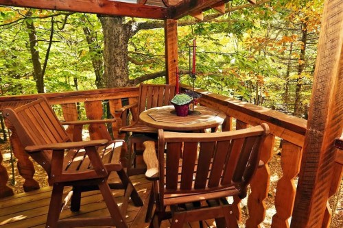 A cozy wooden deck with two chairs and a round table, surrounded by vibrant autumn foliage.