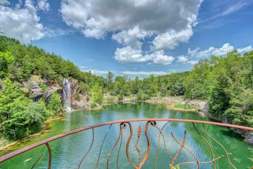 A scenic view of a lush green landscape with a waterfall and a tranquil lake under a blue sky with fluffy clouds.