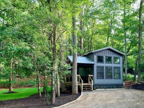 A modern gray house nestled among tall trees, featuring large windows and a welcoming porch.