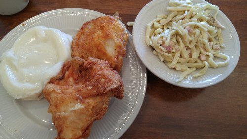 A plate with two pieces of fried chicken, mashed potatoes with gravy, and a side of pasta salad.