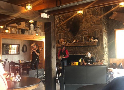 A cozy venue with a stone fireplace featuring a live band playing music, with wooden decor and warm lighting.