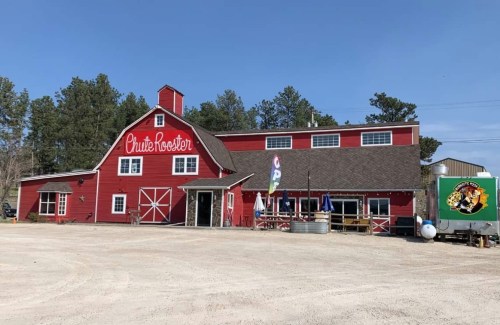 A large red barn-style building with "Chute Rooster" painted on the side, surrounded by trees and a gravel lot.