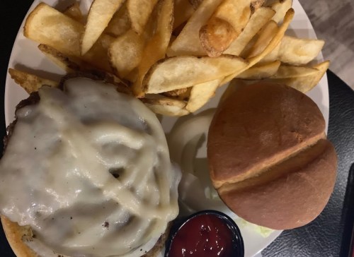 A plate with a cheeseburger topped with melted cheese, a side of fries, and a small bun with a ketchup cup.