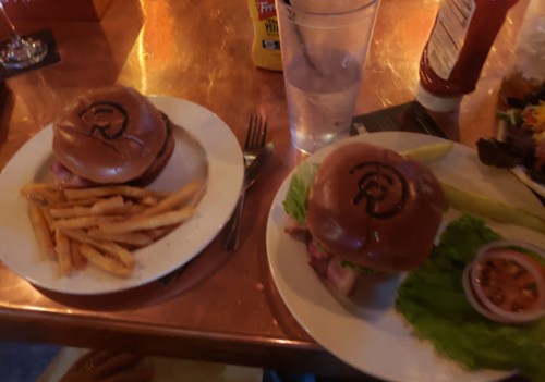 Two plates with burgers and fries on a copper table, one burger topped with lettuce and a side of dipping sauce.