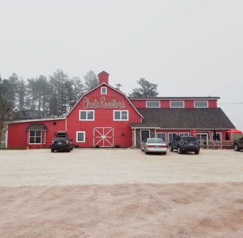 A red barn-style building with "Chute Roosters" sign, surrounded by parked cars and a foggy landscape.