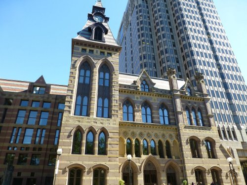 Historic building with ornate architecture, featuring large windows and a clock tower, next to a modern skyscraper.