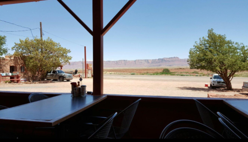 View from a restaurant porch showing a desert landscape, mountains in the distance, and parked vehicles.