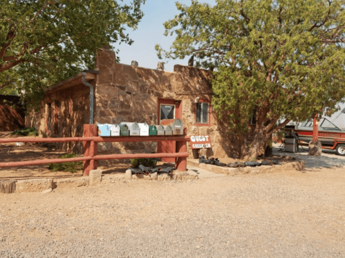 A rustic stone building with a row of mailboxes in front, surrounded by trees and gravel.