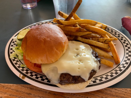 A cheeseburger with melted cheese, lettuce, tomato, and pickles, served with a side of golden fries on a checkered plate.
